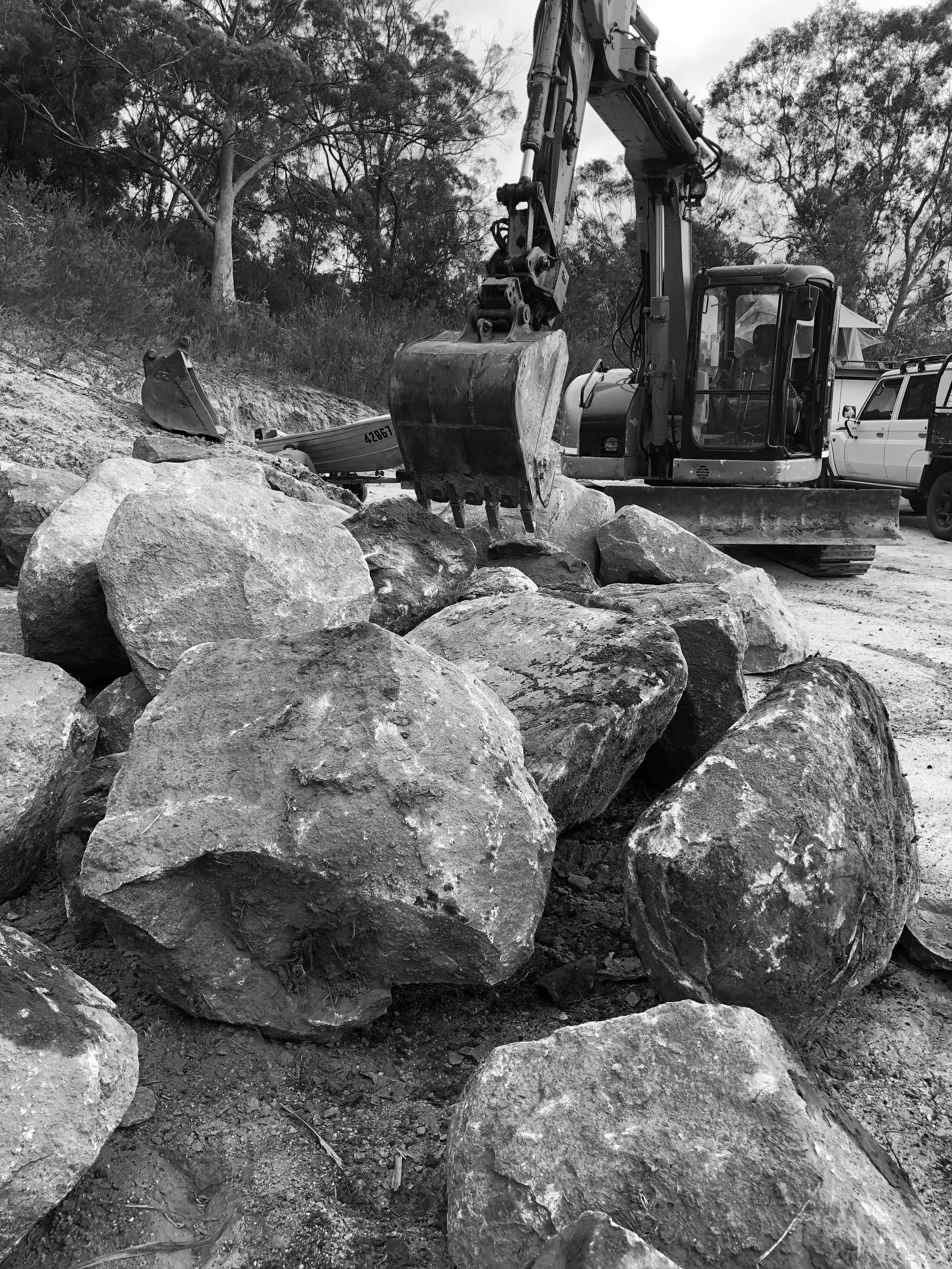 Excavator arranging granite rocks on the site